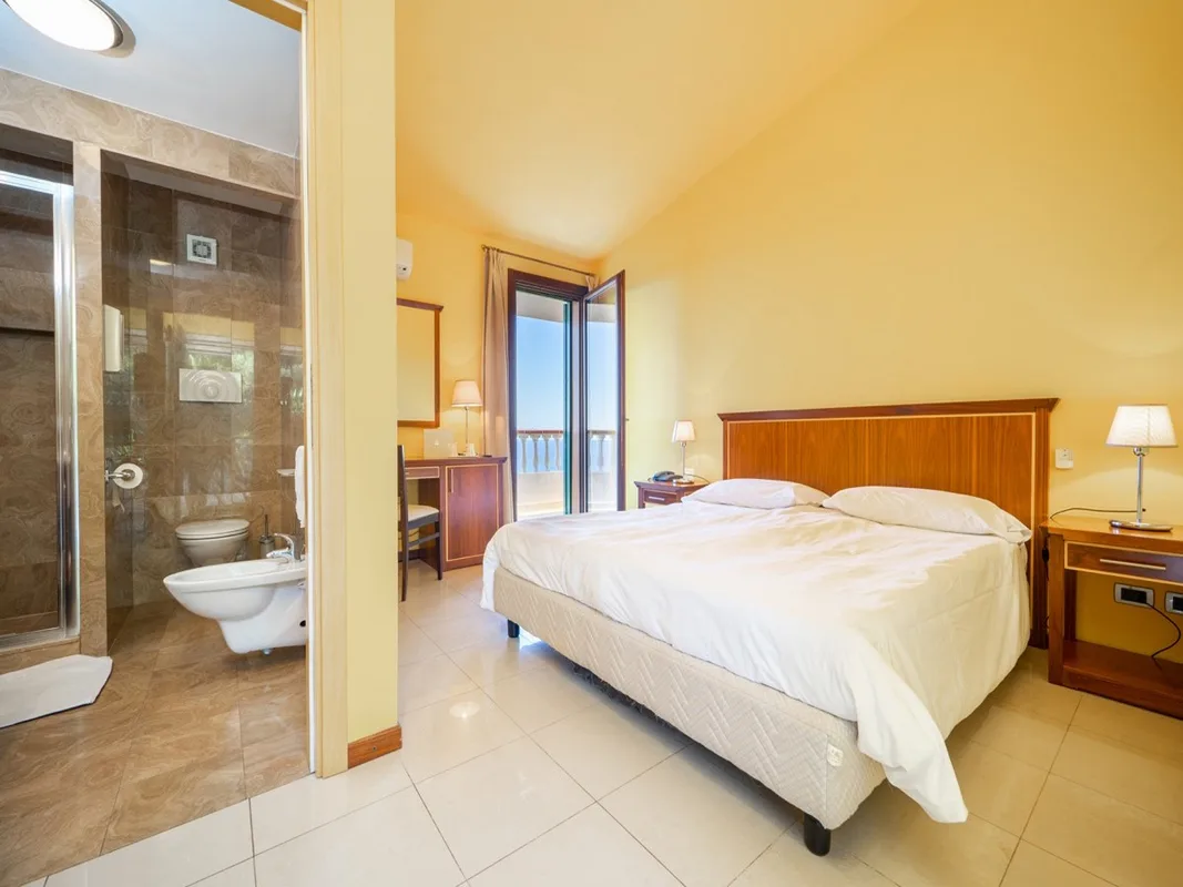 Camera matrimoniale con pareti gialle, bagno con doccia e balcone affacciato sulla vista