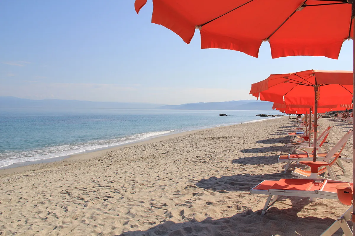 Vista del mare calmo dalla spiaggia con ombrelloni rossi e lettini arancioni