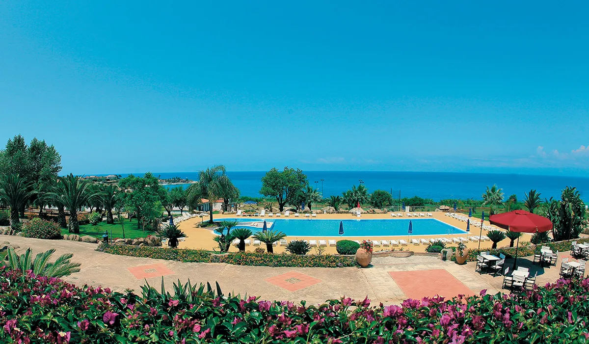 Veduta panoramica della piscina del resort con giardino, palme e mare all'orizzonte