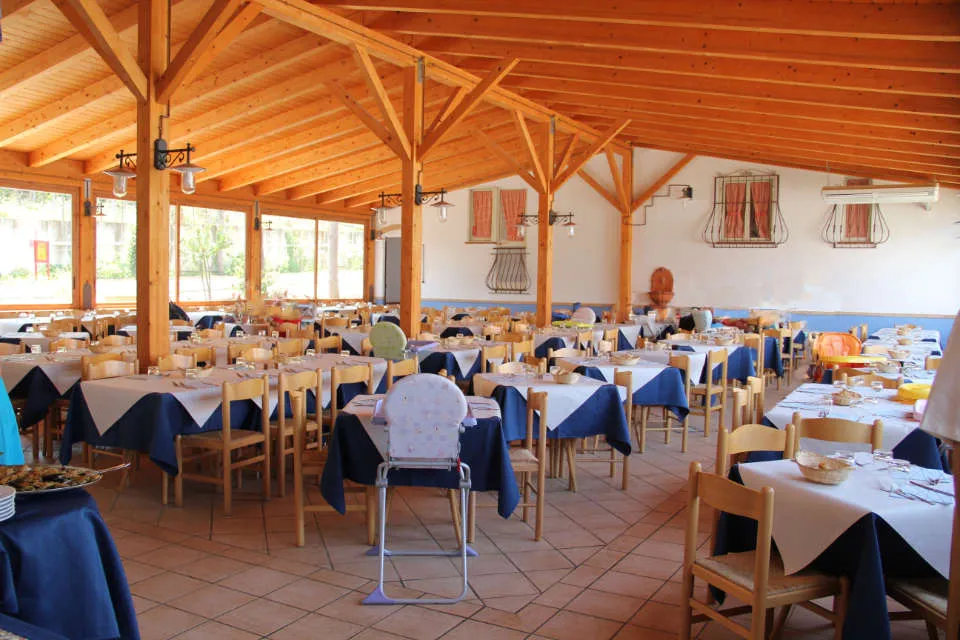 Sala ristorante interna con travi in legno, tavoli apparecchiati e seggiolone