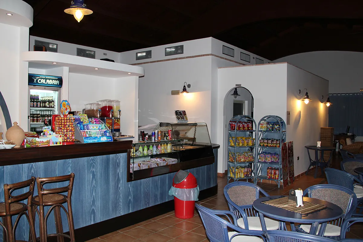 Bar interno con bancone, frigorifero bevande, snack e tavolini in vimini