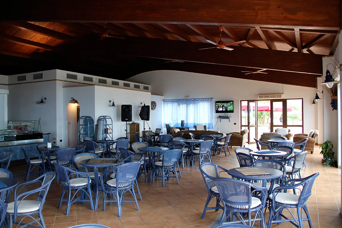 Sala bar con soffitto in legno, tavoli e sedie in vimini blu e zona TV