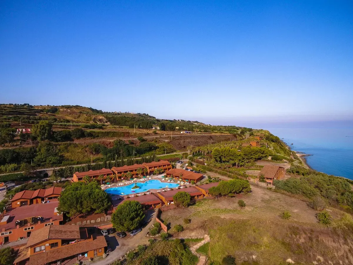 Panorama aereo del villaggio con piscina centrale immerso nel verde sulla costa