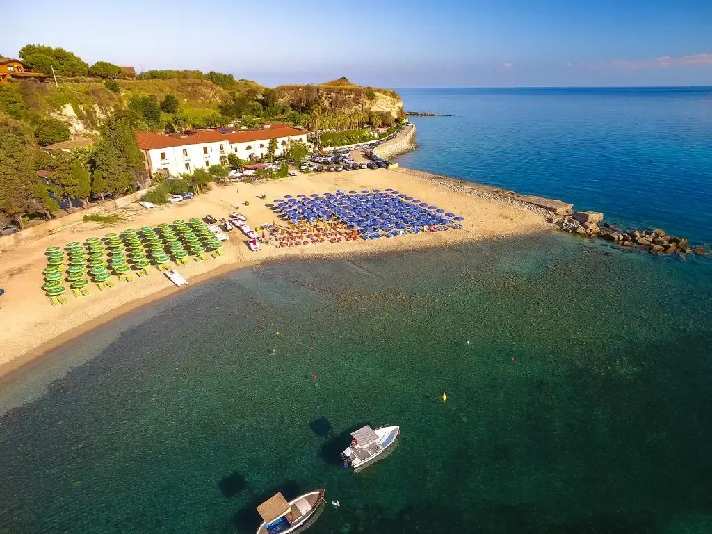 Spiaggia con file di ombrelloni colorati e barche ancorate nel mare limpido