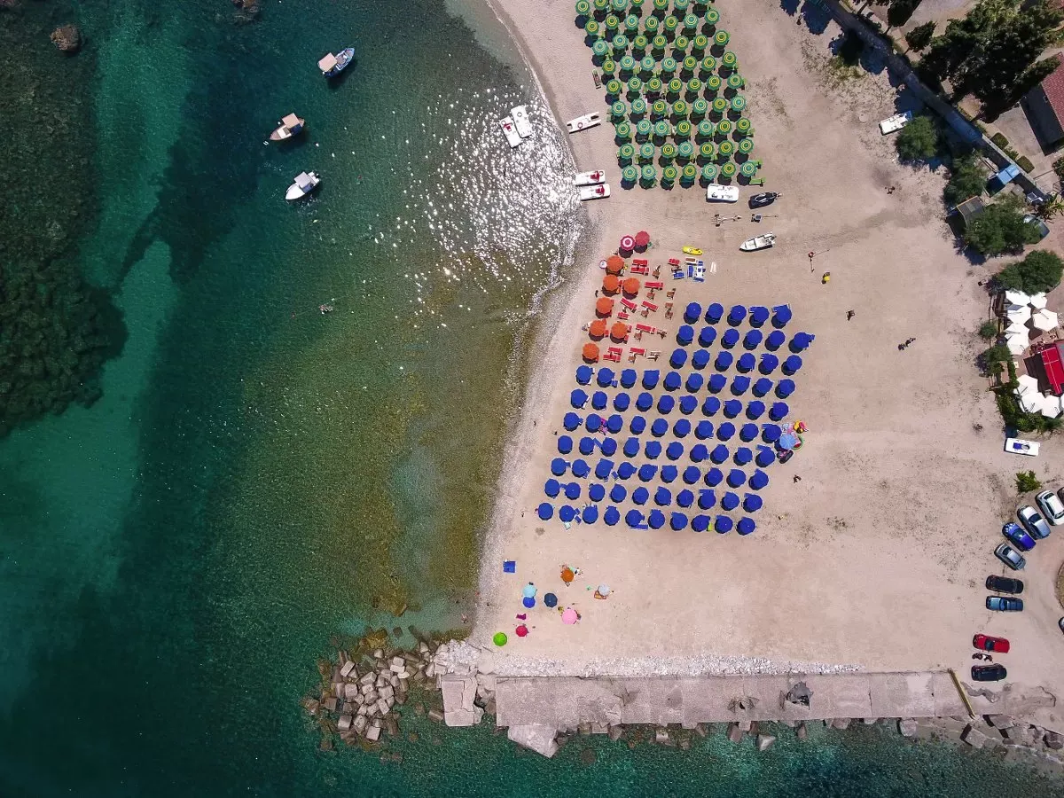 Veduta aerea della spiaggia con ombrelloni blu e verdi e barche nel mare