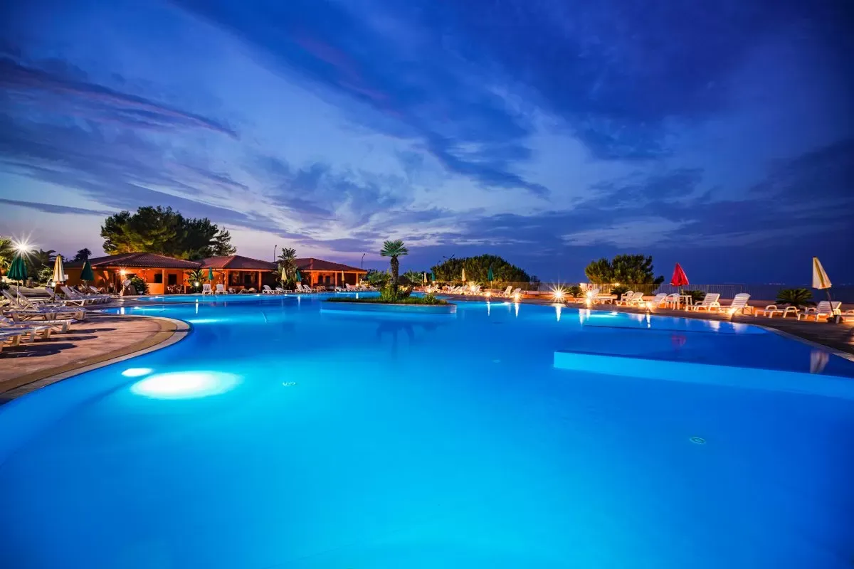 Piscina illuminata di sera con cielo blu intenso e luci che si riflettono nell'acqua