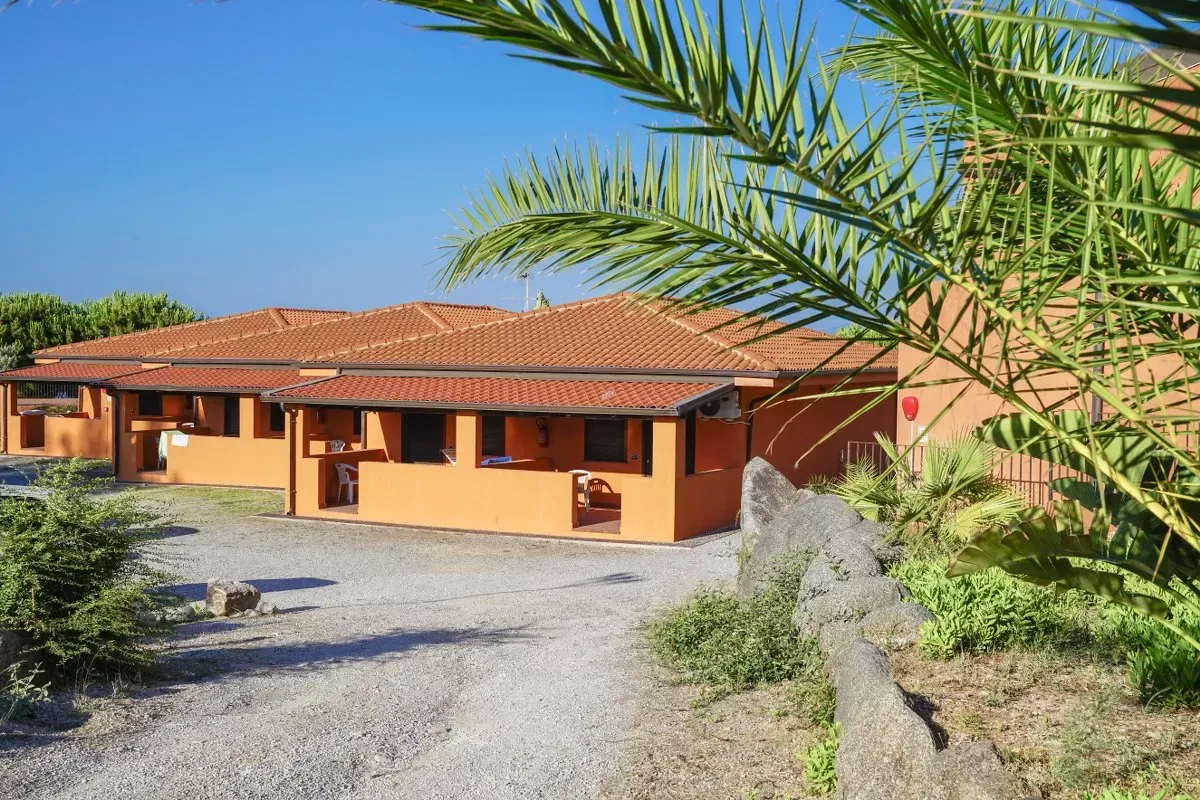 Esterno delle villette arancioni del resort con tetti in tegole e palma in primo piano