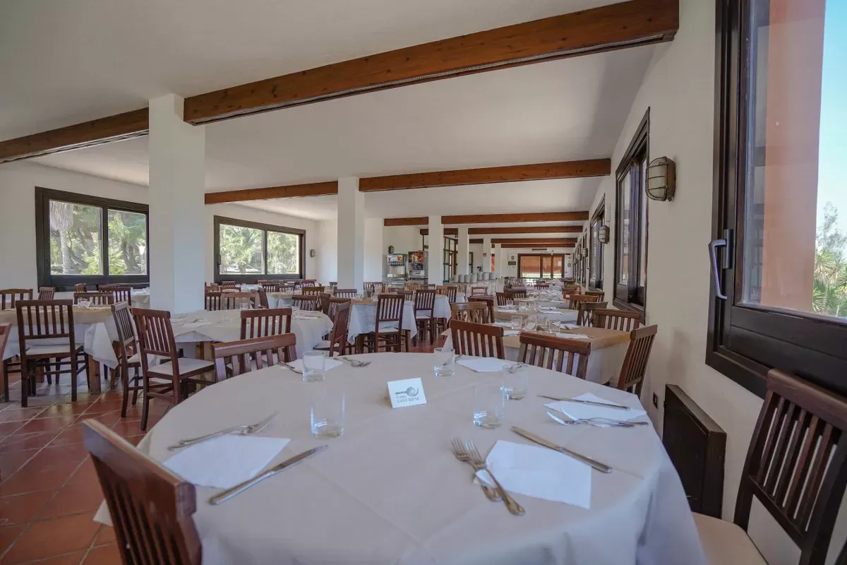 Sala ristorante interna con tavoli rotondi e rettangolari apparecchiati e travi in legno