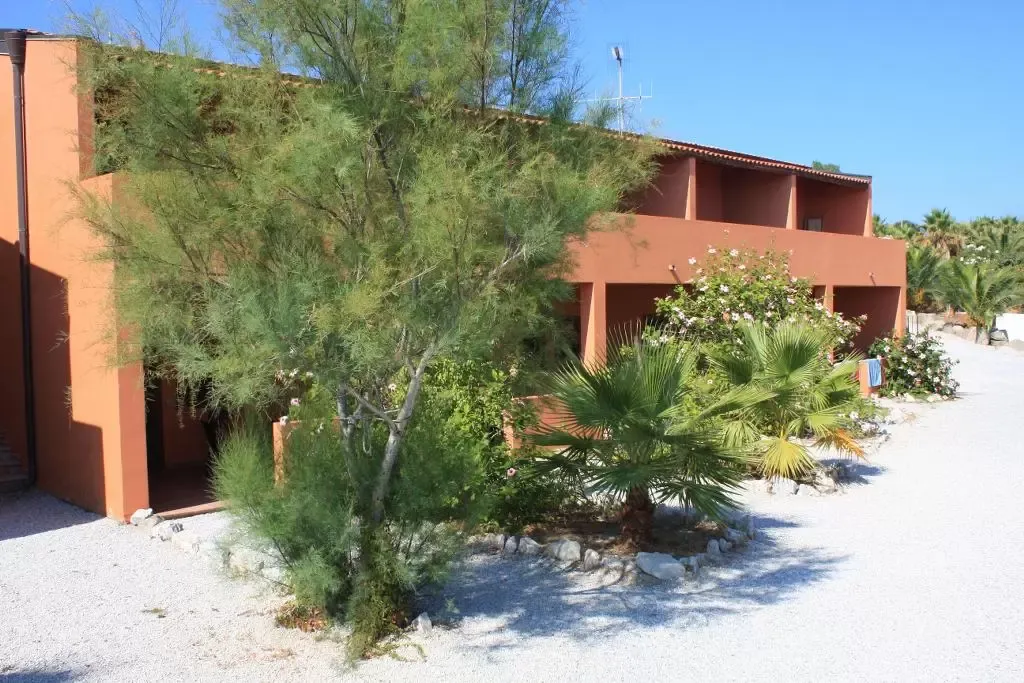 Esterno di una villetta arancione del resort circondata da vegetazione e ghiaia