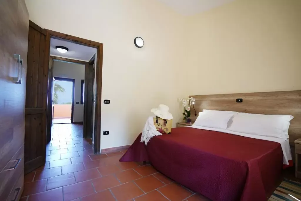 Camera matrimoniale con copriletto bordeaux, armadio in legno e ingresso luminoso