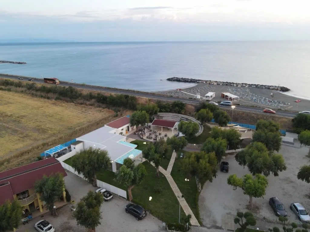 Veduta aerea del resort con piscina, giardino e spiaggia affacciata sul mare al tramonto