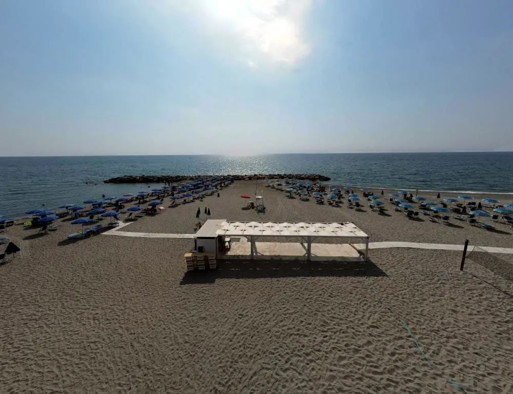 Spiaggia di sabbia con gazebo bianco, ombrelloni blu e mare illuminato dal sole