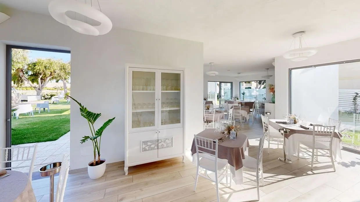 Sala ristorante in stile chiaro con tavoli apparecchiati, vetrina e affaccio sul giardino