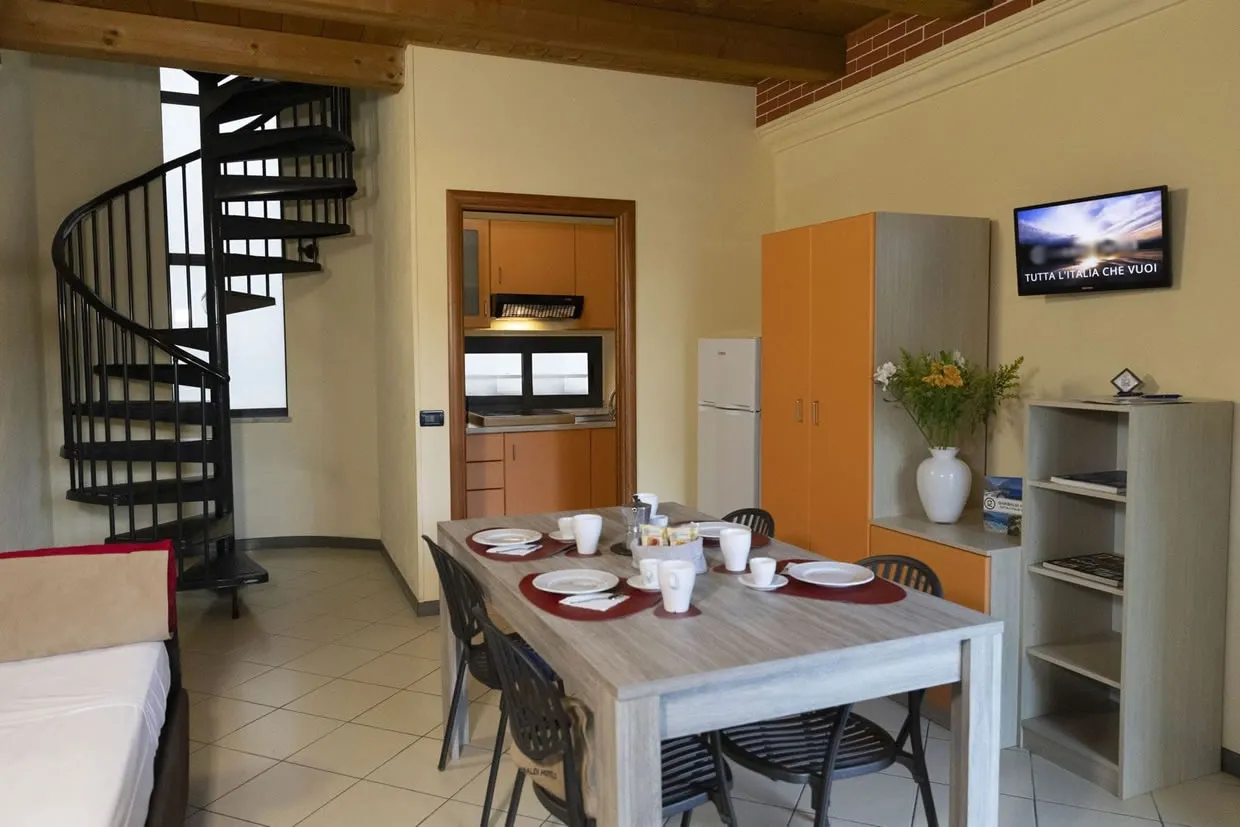 Appartamento con angolo cottura, tavolo apparecchiato, scala a chiocciola e TV