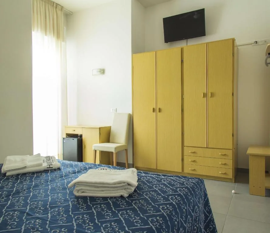 Camera con letto matrimoniale blu, armadio in legno chiaro, TV e scrivania con sedia