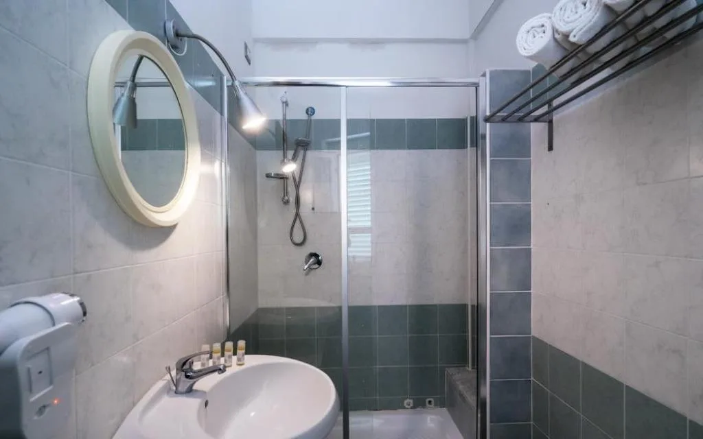 Bagno con doccia, lavabo, specchio rotondo e piastrelle verdi e bianche