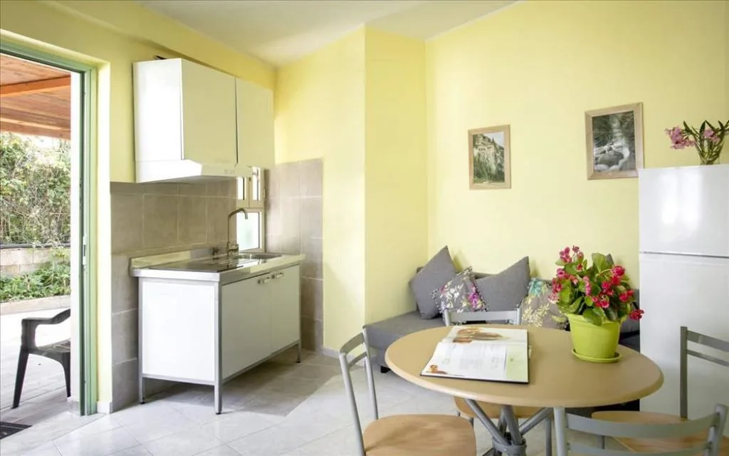 Angolo cottura con cucina compatta, divano grigio e tavolo da pranzo in ambiente giallo