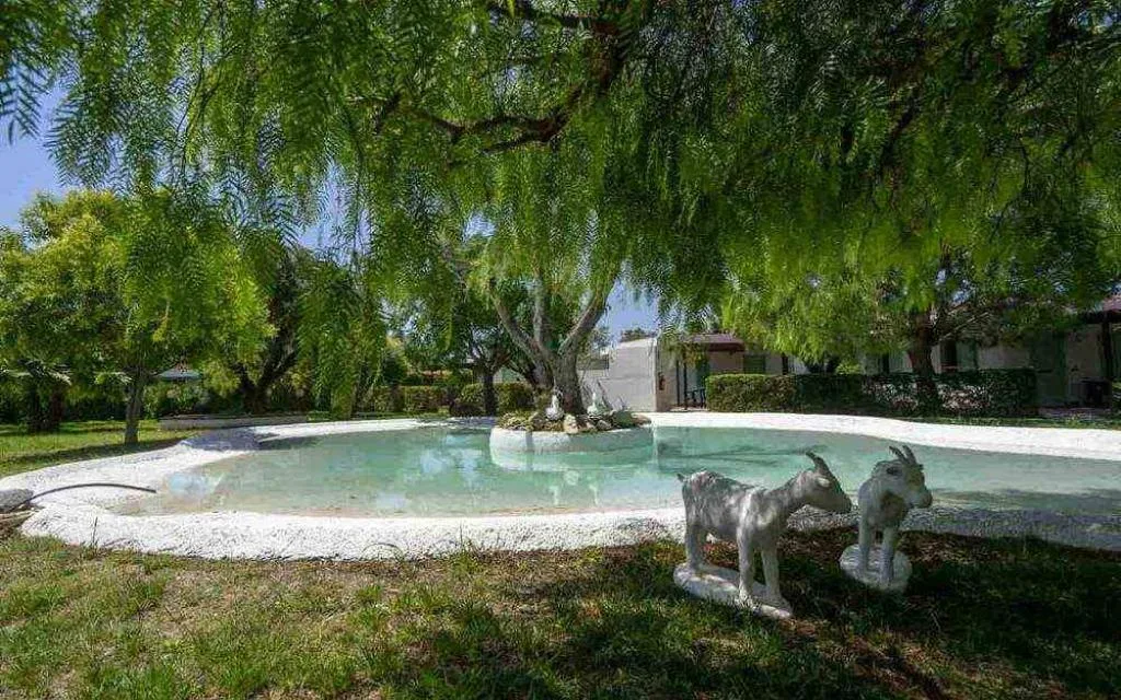 Giardino con laghetto, alberi ombrosi e sculture di capre in pietra
