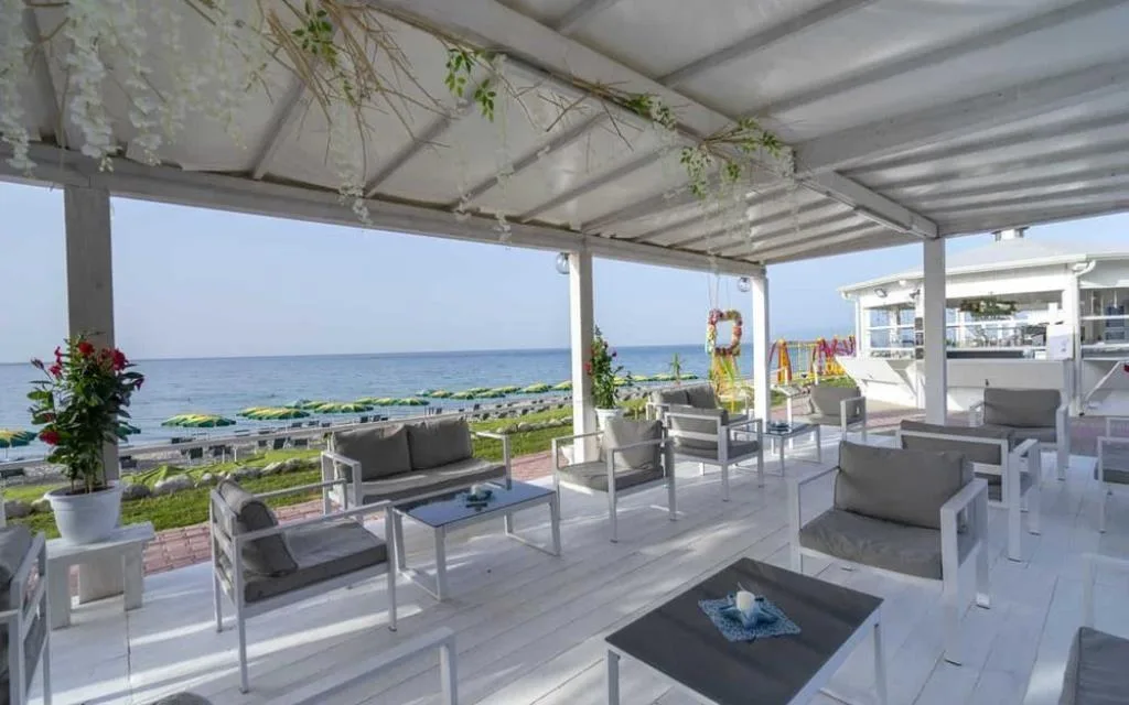 Lounge coperto sul mare con divani grigi, decorazioni floreali e vista sulla spiaggia