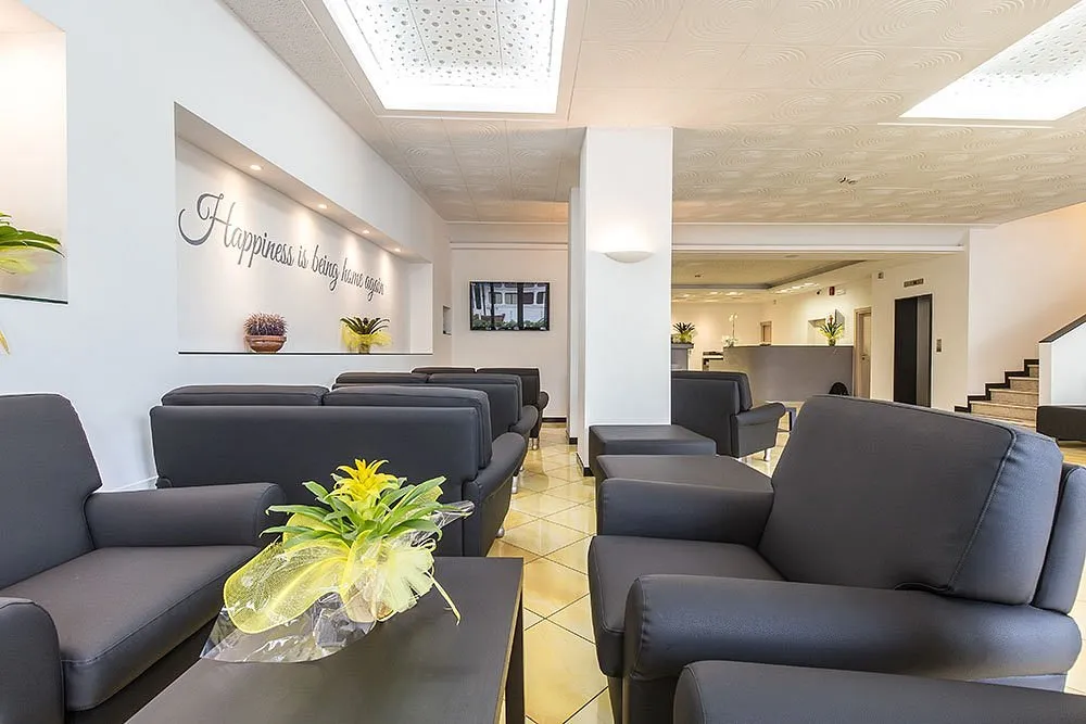Hall dell'hotel con poltrone grigie, scritta decorativa a parete e reception sullo sfondo