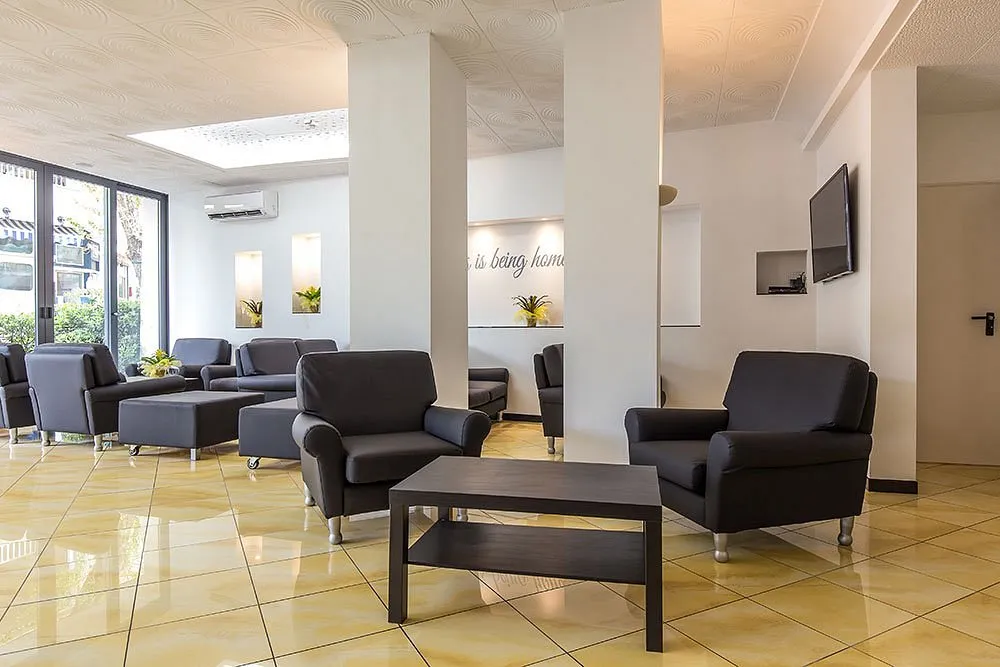 Area lounge della hall con poltrone grigie, tavolino, TV a parete e pavimento in piastrelle chiare