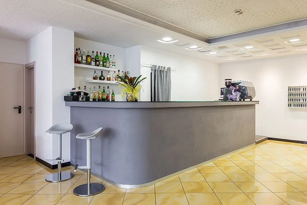 Bancone bar dell'hotel con sgabelli, bottiglie di liquori e macchina del caffè professionale