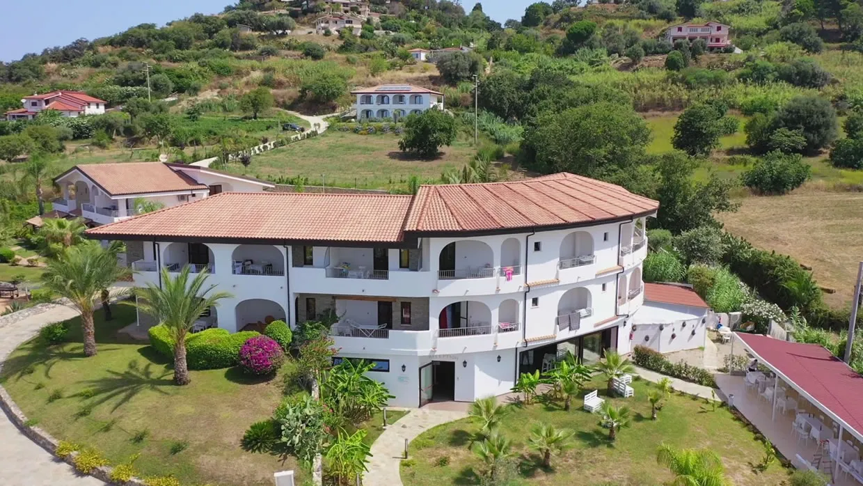 Edificio bianco del resort dal tetto rosso con balconi ad arco immerso nel verde collinare
