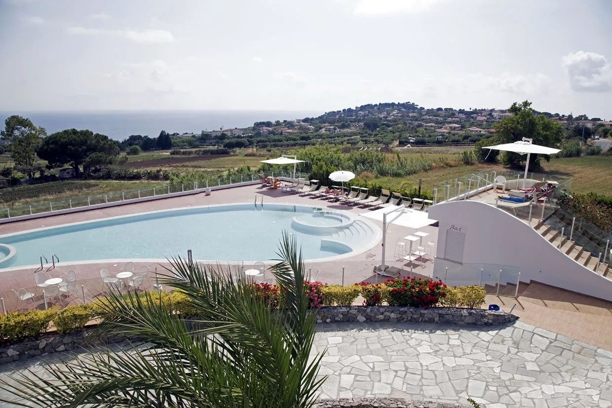 Piscina del resort con area bar bianca, ombrelloni e vista sulla campagna e il mare