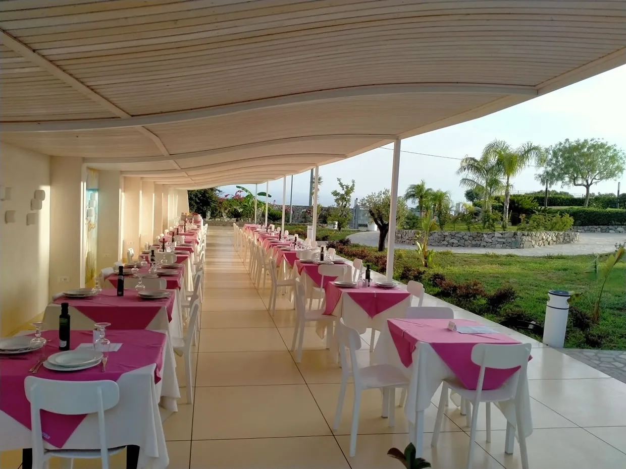 Ristorante all'aperto con tavoli apparecchiati e tovaglie fucsia sotto pergolato bianco