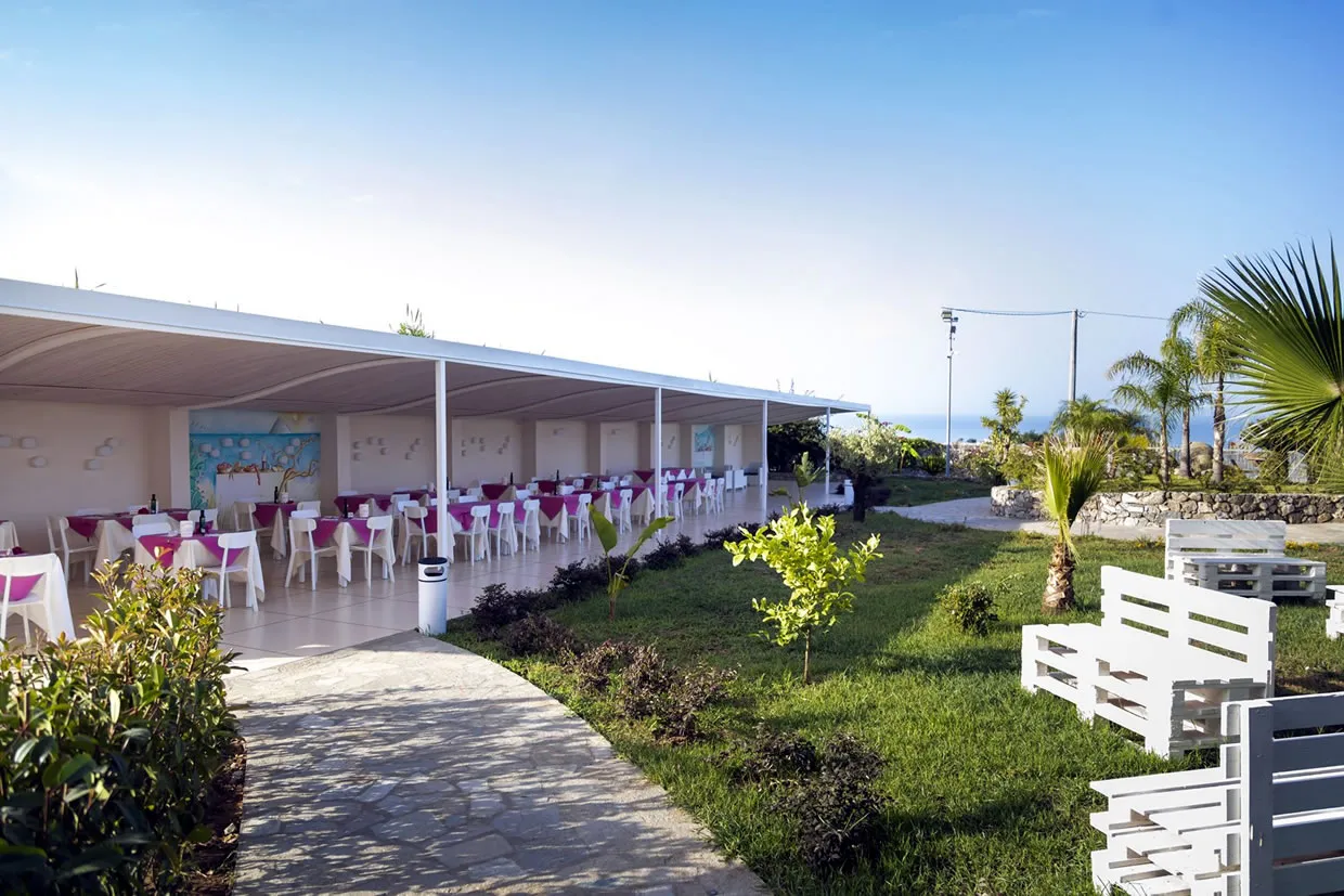 Sala ristorante coperta con tavoli apparecchiati e giardino con vista mare