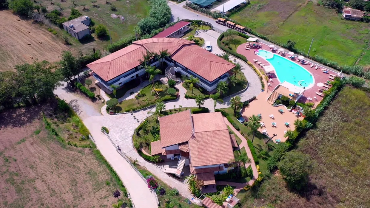 Veduta aerea ravvicinata del resort con edifici dai tetti rossi, piscina e giardini