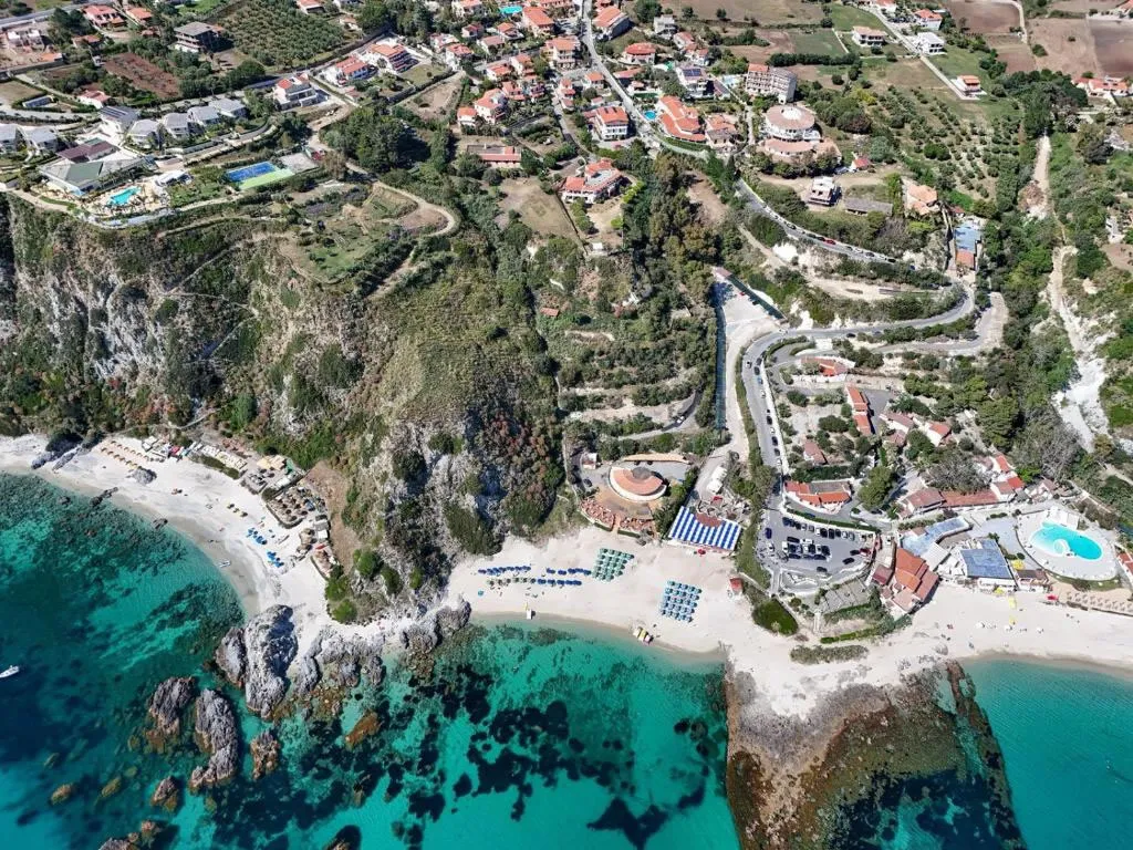 Vista aerea della costa con spiaggia, mare cristallino turchese e abitato sulla scogliera