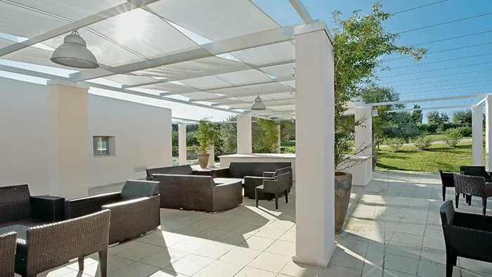 Area lounge esterna con divani sotto pergolato bianco e vista sul giardino