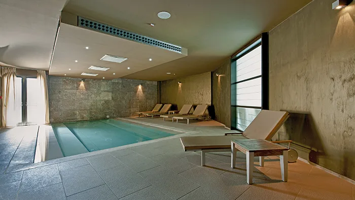 Piscina coperta con lettini e pareti in cemento