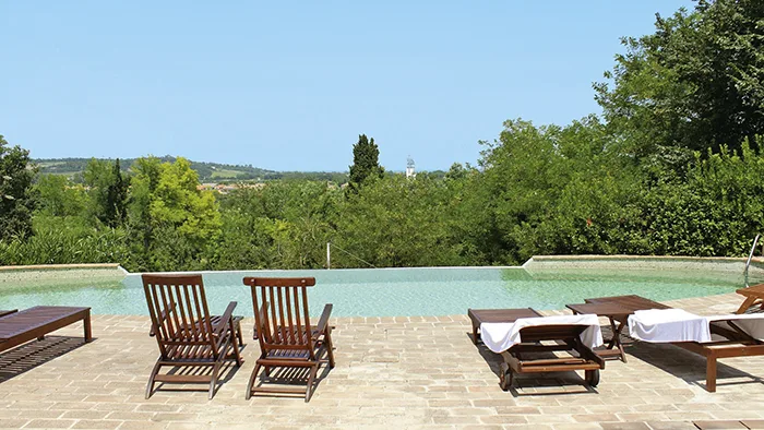 Piscina a sfioro con lettini in legno affacciata sulle colline verdi