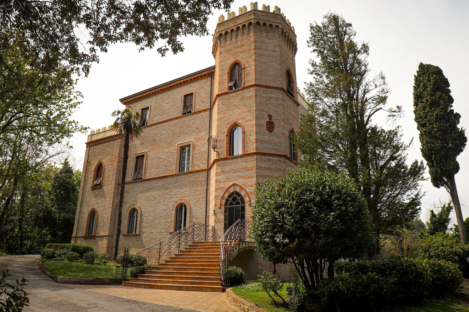 Imponente castello in mattoni con torre merlata, scalinata d'ingresso e giardino curato