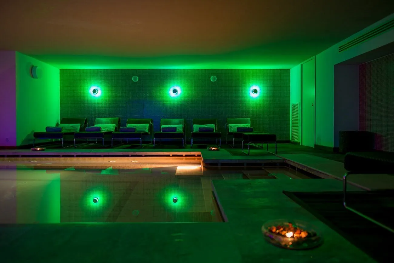 Zona relax della spa con illuminazione verde, vasca idromassaggio e lettini