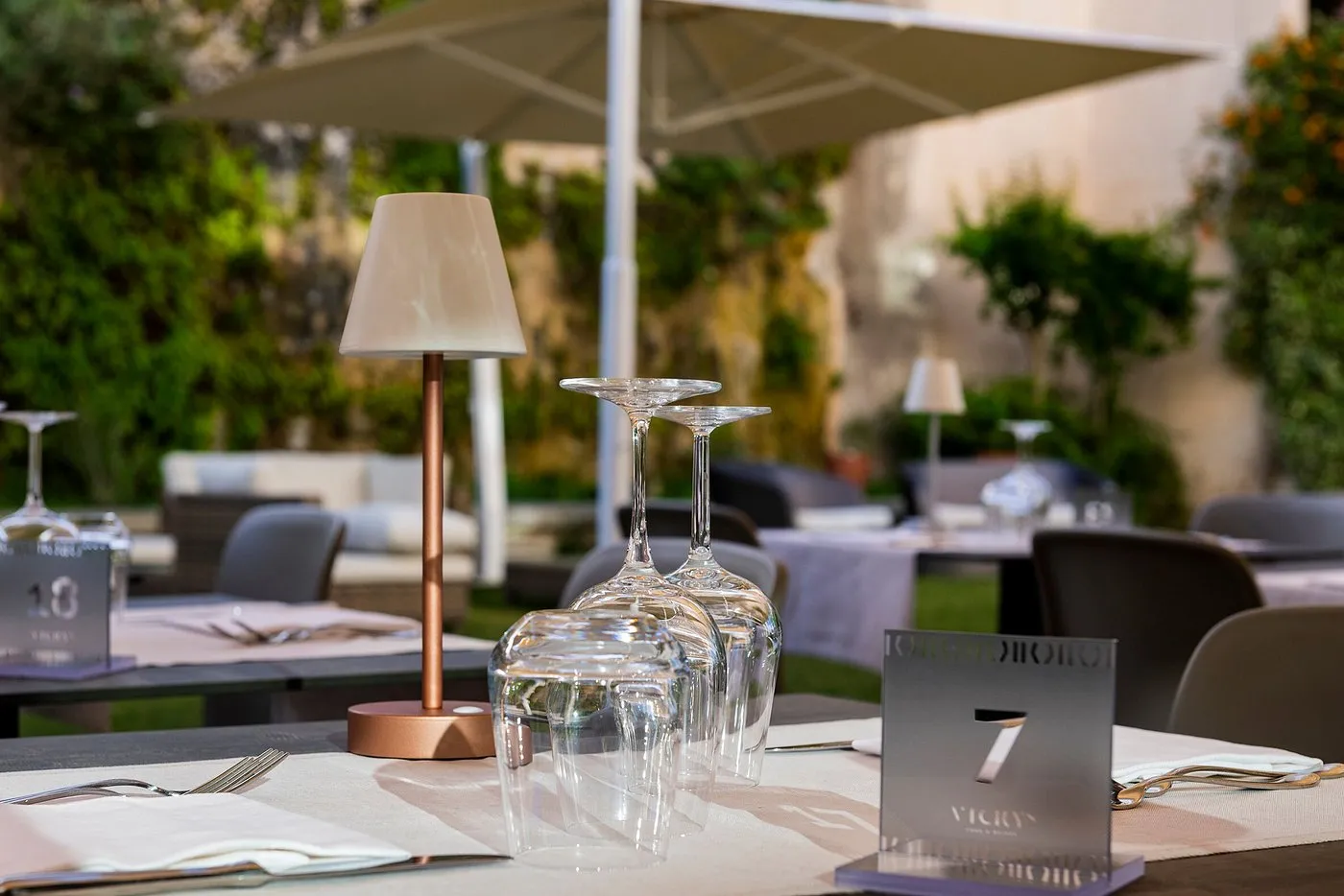 Tavolo apparecchiato del ristorante all'aperto con calici e lampada da tavolo