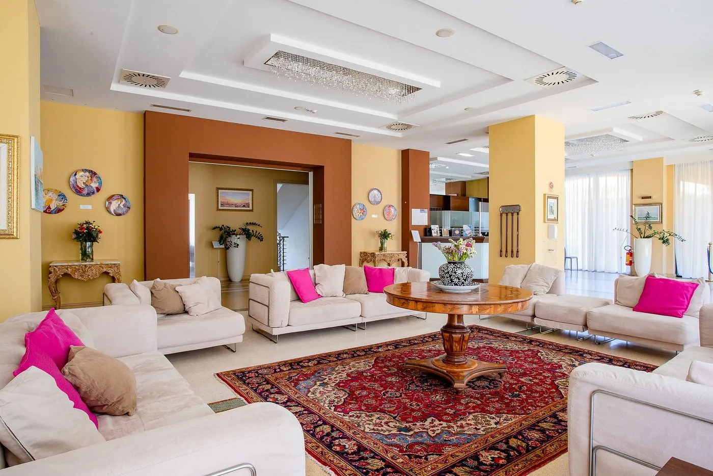 Hall dell'hotel con divani bianchi, cuscini fucsia, tappeto orientale e tavolo in legno