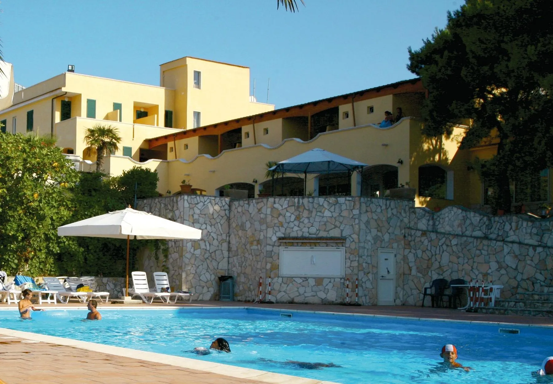 Piscina con bagnanti e edificio giallo dell'hotel sullo sfondo