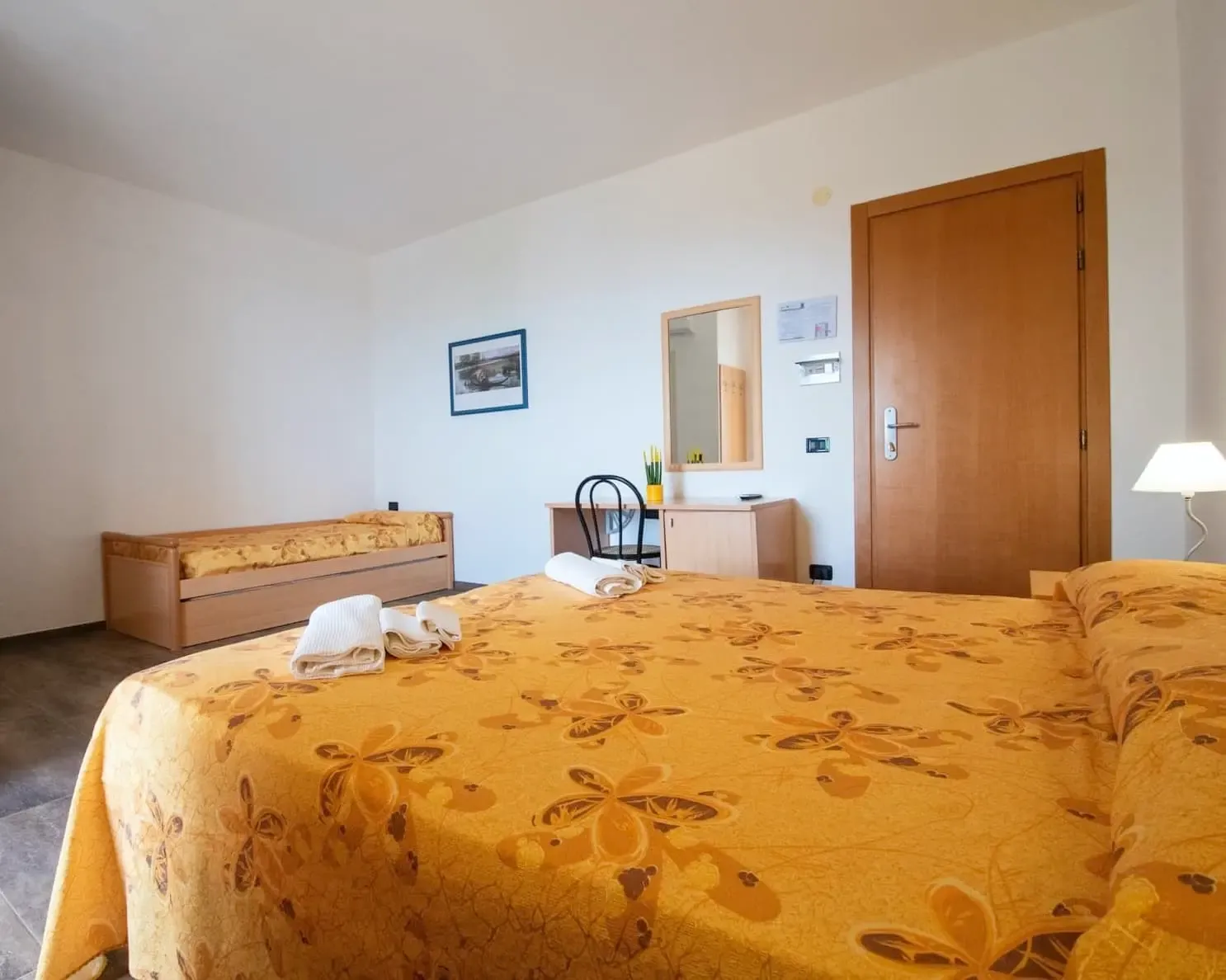 Camera matrimoniale con copriletto giallo a fiori e letto singolo aggiuntivo