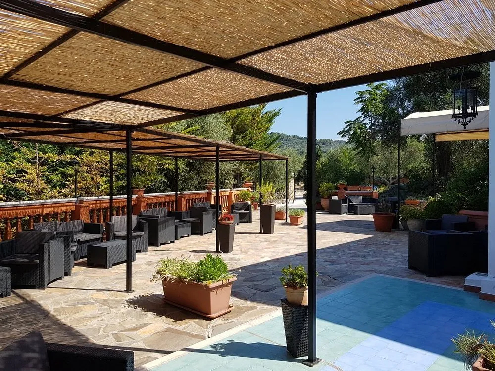 Area lounge esterna con divani scuri sotto pergolato in canne
