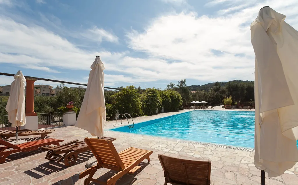 Piscina con lettini in legno e ombrelloni chiusi sotto cielo nuvoloso