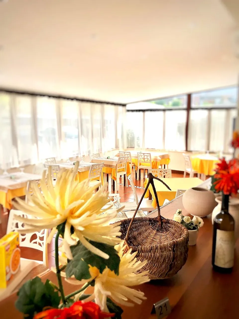 Interno del ristorante con tavoli apparecchiati, cesto in vimini e fiori in primo piano