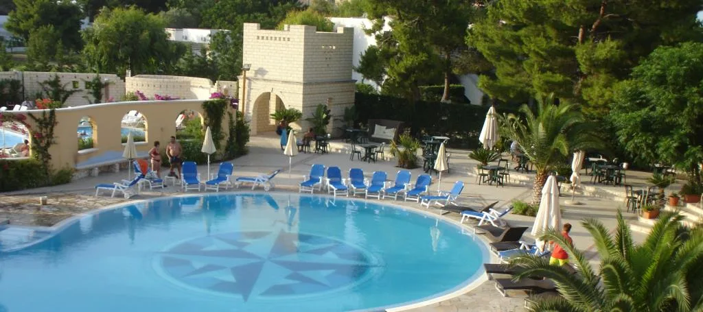 Piscina con rosa dei venti sul fondo, lettini blu e palme circostanti