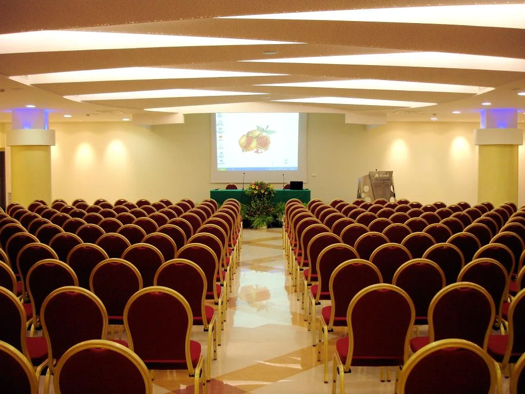 Sala conferenze con sedie rosse disposte in file e schermo per proiezioni