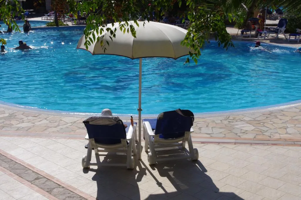 Due lettini con ombrellone bianco a bordo piscina con bagnanti in acqua