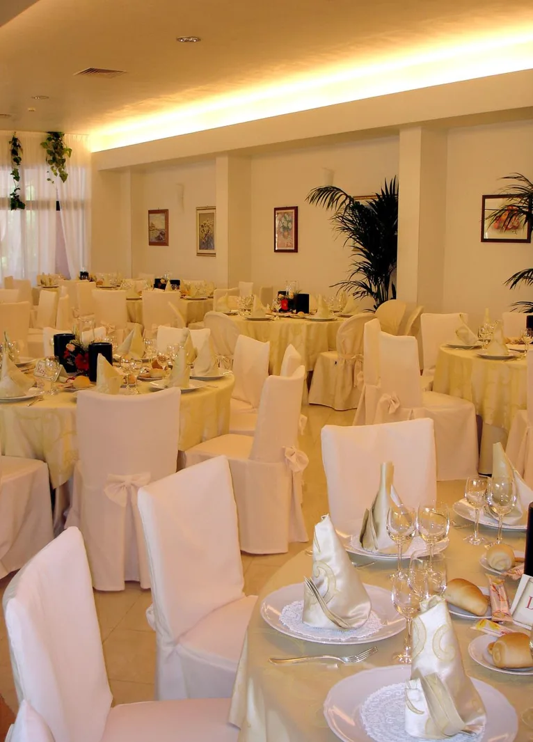 Sala ristorante elegante con tavoli rotondi apparecchiati e sedie con coprisedia bianchi