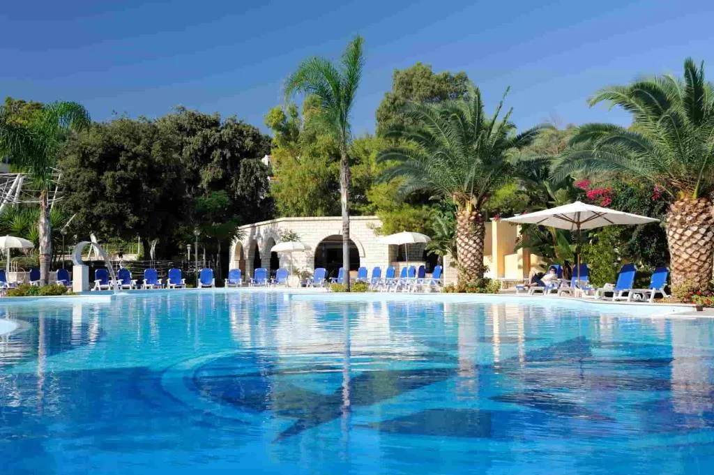 Ampia piscina azzurra con lettini blu e palme che si riflettono nell'acqua