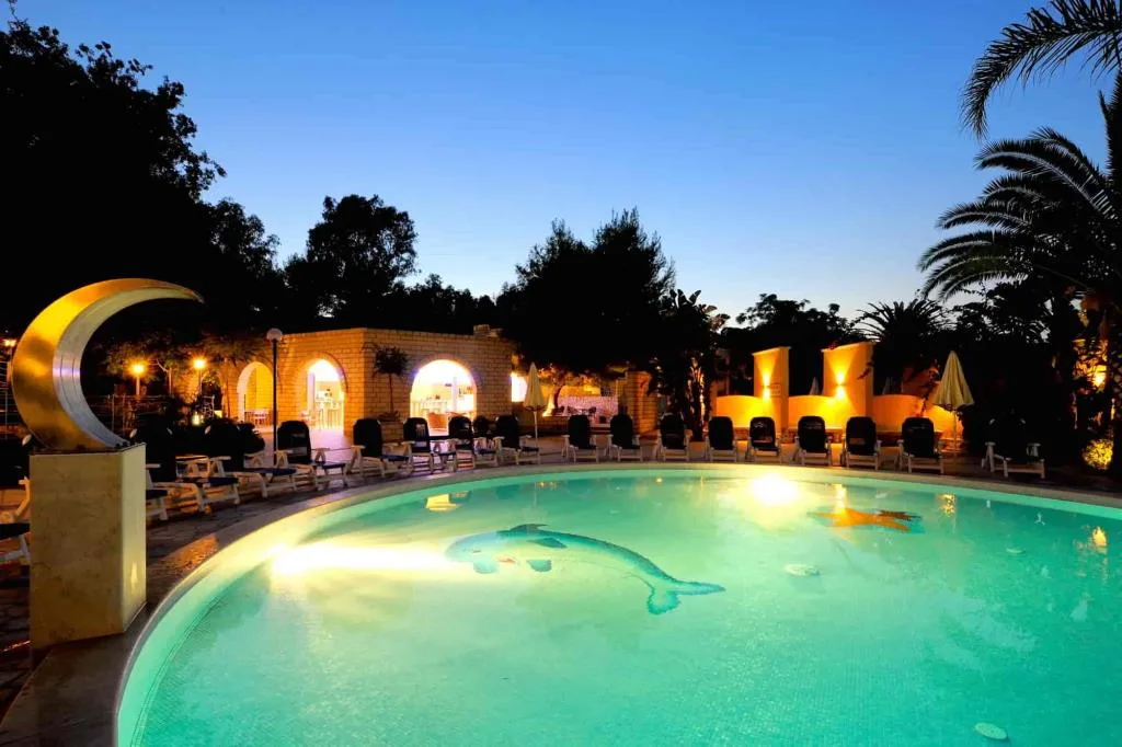 Piscina illuminata di sera con decorazione a delfino sul fondo e scultura a luna crescente